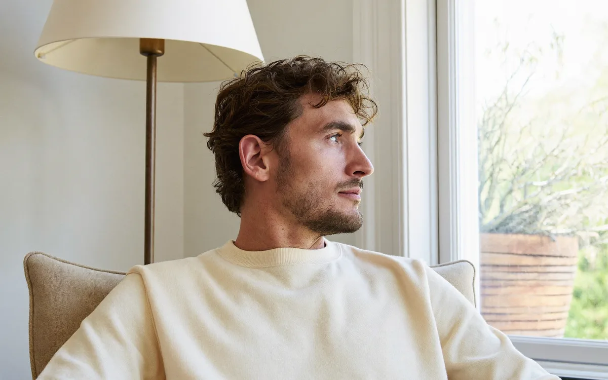 A man sitting in a bright room by a window, relaxed, looking outside