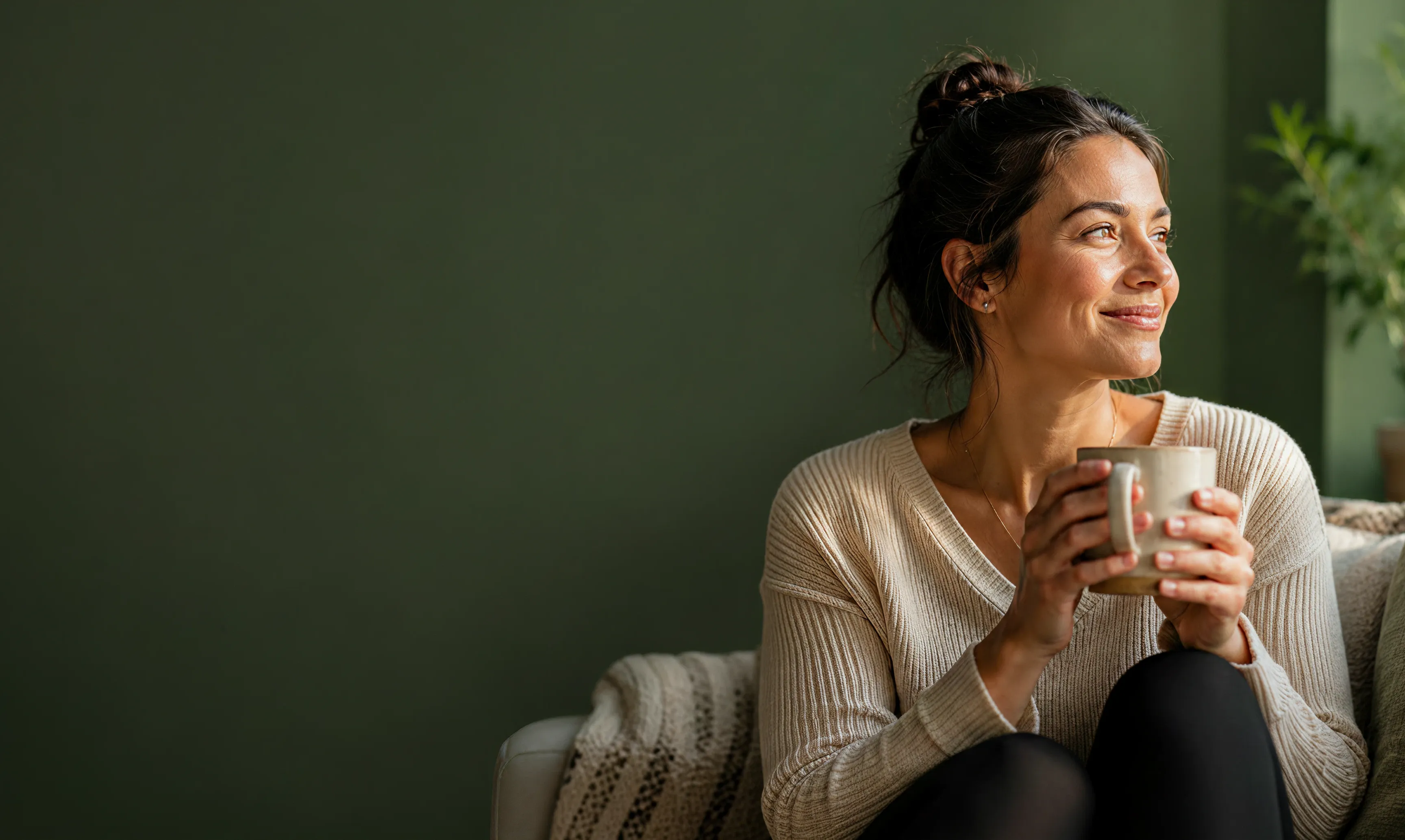 A woman smiling while holding a warm mug in soft natural light